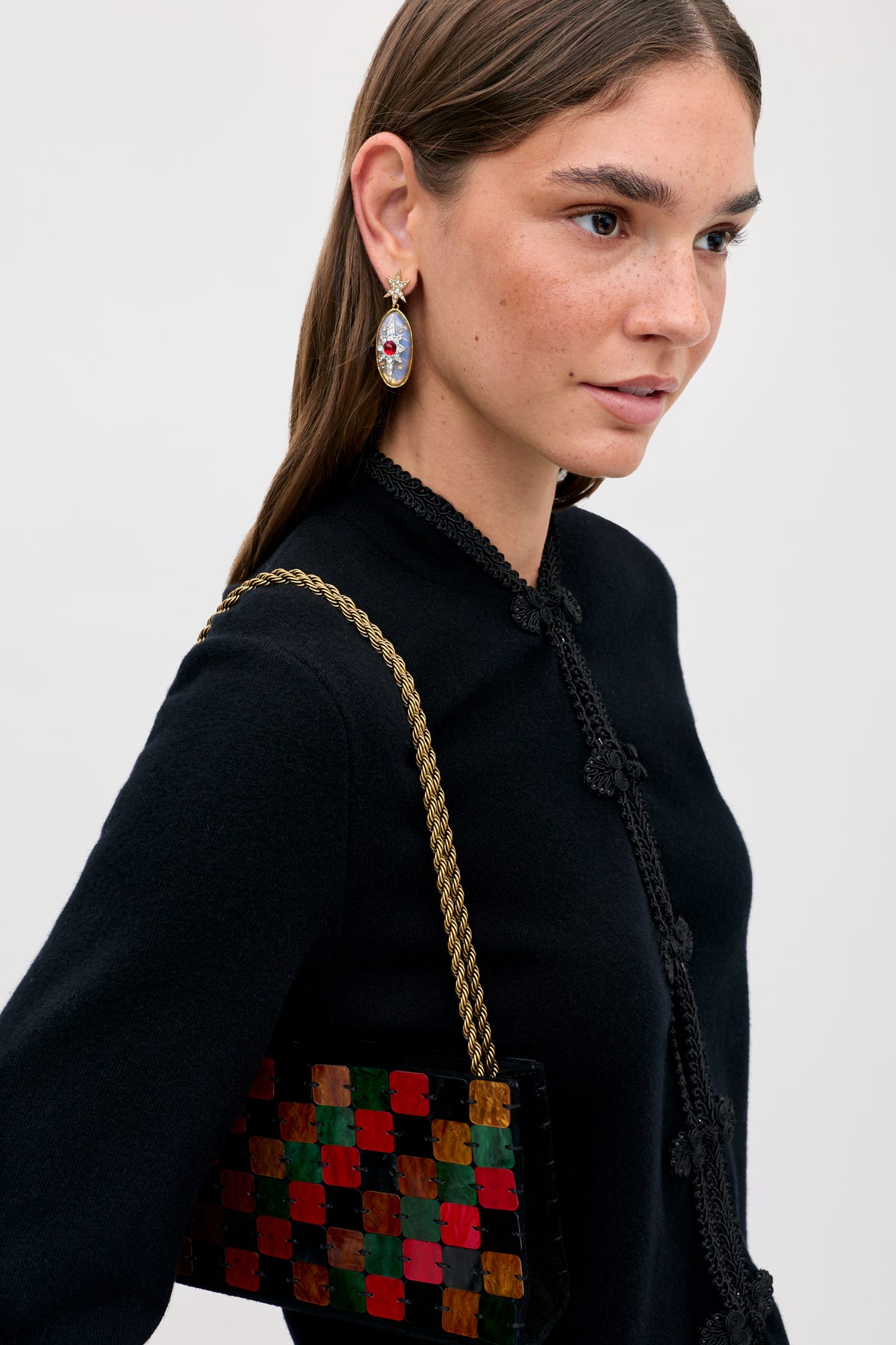 A woman wears a black top and a Gracelyn - Multi handbag featuring a multicolored checkerboard pattern and a gold chain strap.