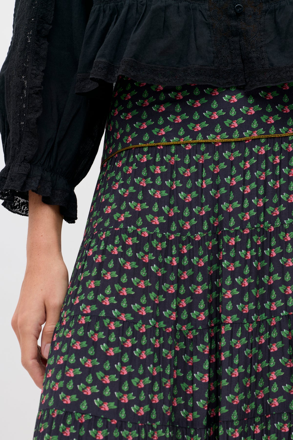 Joey - Mini Rose Pink tiered black skirt featuring a repeating pattern of small pink roses and green leaves, worn with a black blouse with lace-trimmed sleeves.