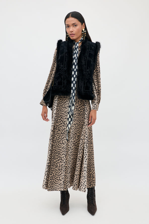 A model wears a leopard print midi dress with a polka dot necktie, a Taletha - Botanical Vine Embroidery Black vest with faux fur trim, and dark brown ankle boots.