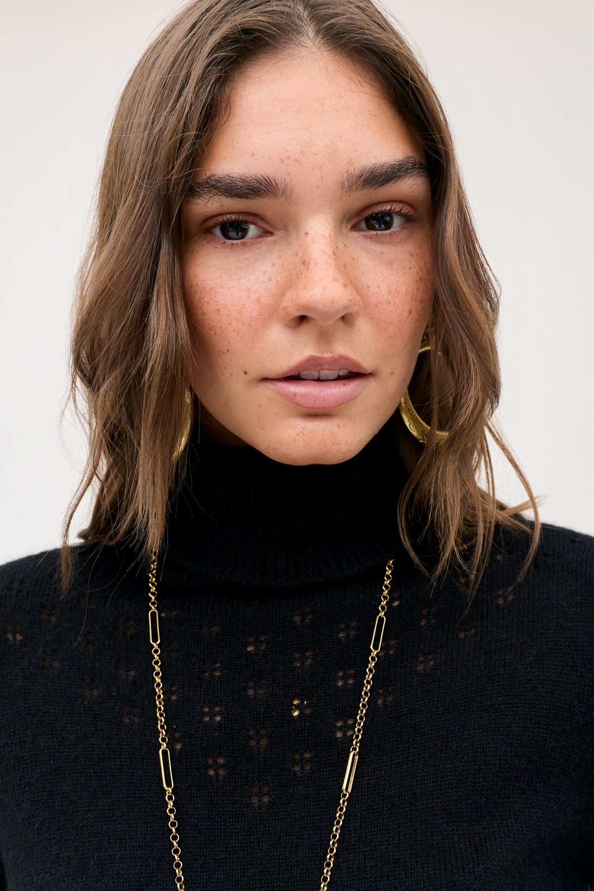 A person wearing a Maryam - Black turtleneck sweater and a long gold chain necklace.