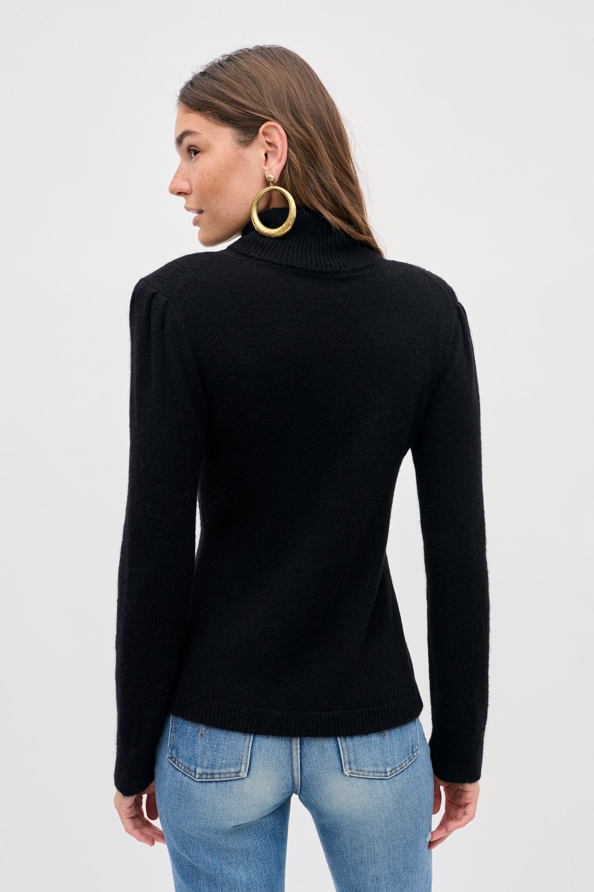 A person seen from behind, wearing a Maryam - Black long-sleeved turtleneck sweater and blue jeans.