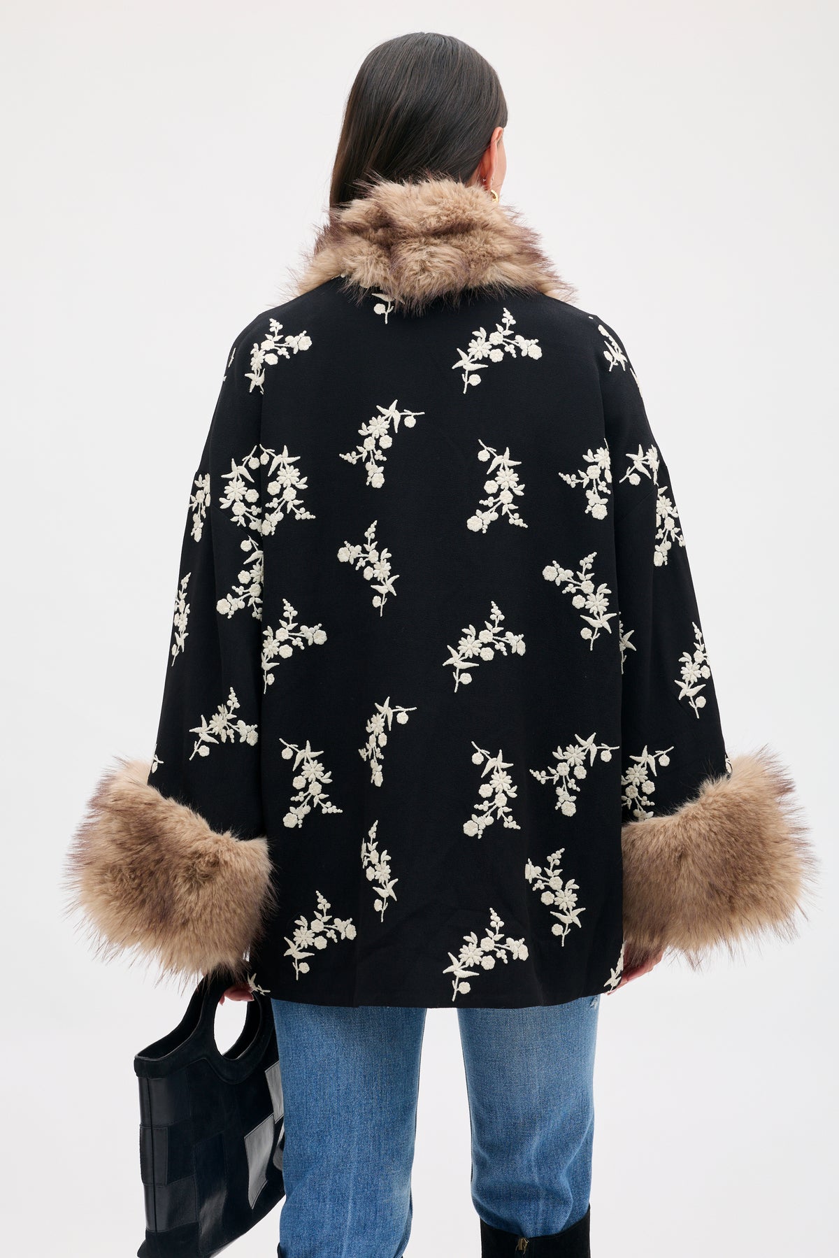 Back view of a person wearing a Micah - Alexa Flower Embroidery Black jacket with cream floral embroidery, a faux fur collar, and faux fur cuffs.