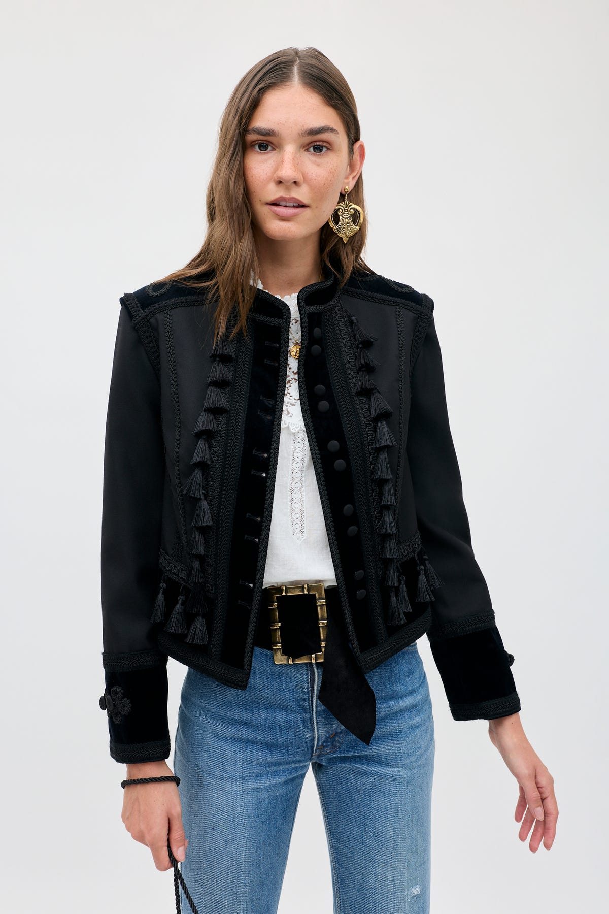 A woman wearing a Napoleana - Black jacket with tassels and velvet trim over a white blouse and blue jeans.
