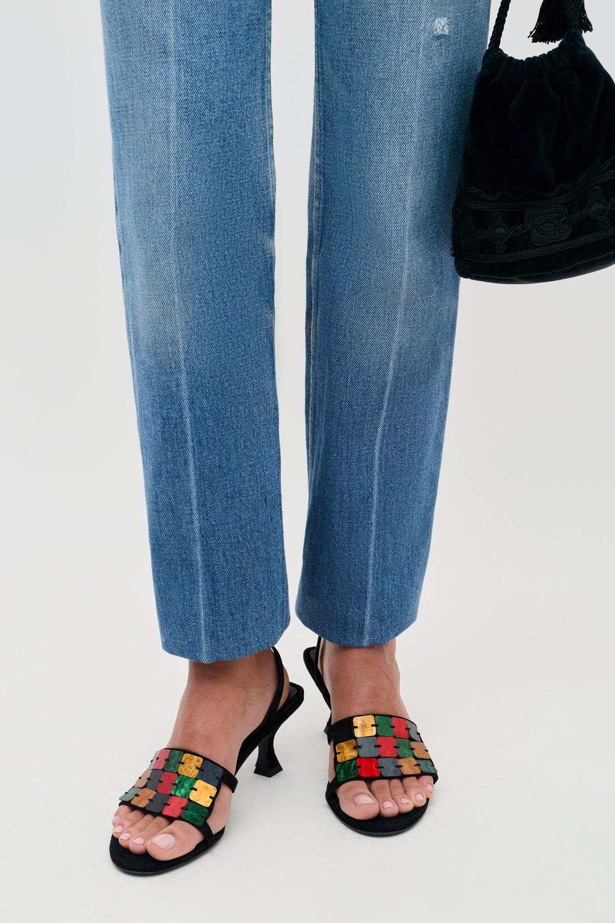 Indie - Multi black slingback sandals featuring a strap of colorful, jigsaw-shaped embellishments, worn with blue jeans and a black handbag.