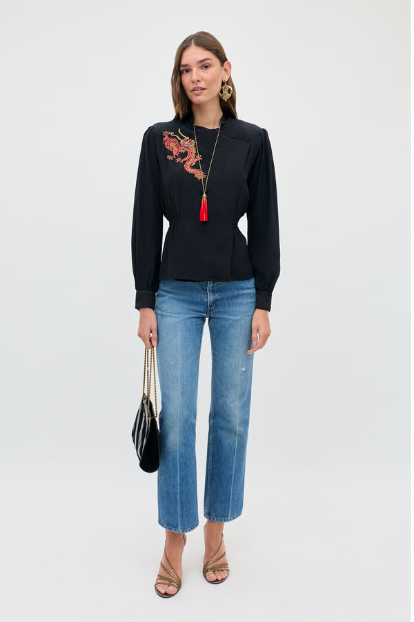 A model wears the Sylvie Rose - Dragon Embroidery Red black long-sleeved blouse, paired with straight-leg blue jeans, a small shoulder bag, and strappy sandals.