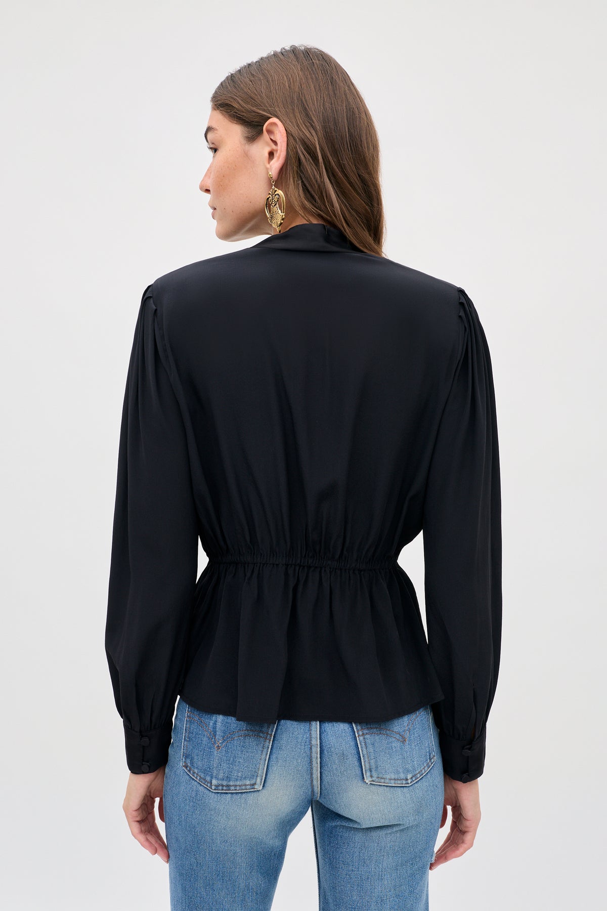 Back view of a person wearing a black long-sleeved Sylvie Rose - Dragon Embroidery Red blouse with a cinched waist and blue jeans.