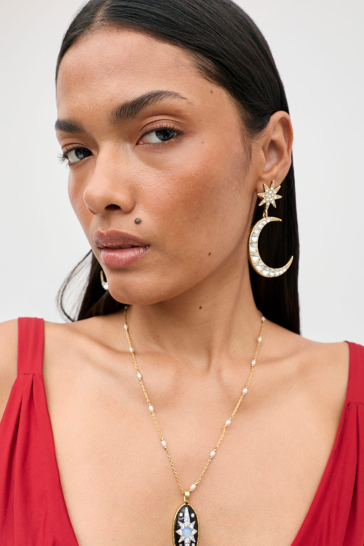 A woman wearing the Theresa - Gold necklace with a celestial pendant and dangling moon and star earrings set with crystals.