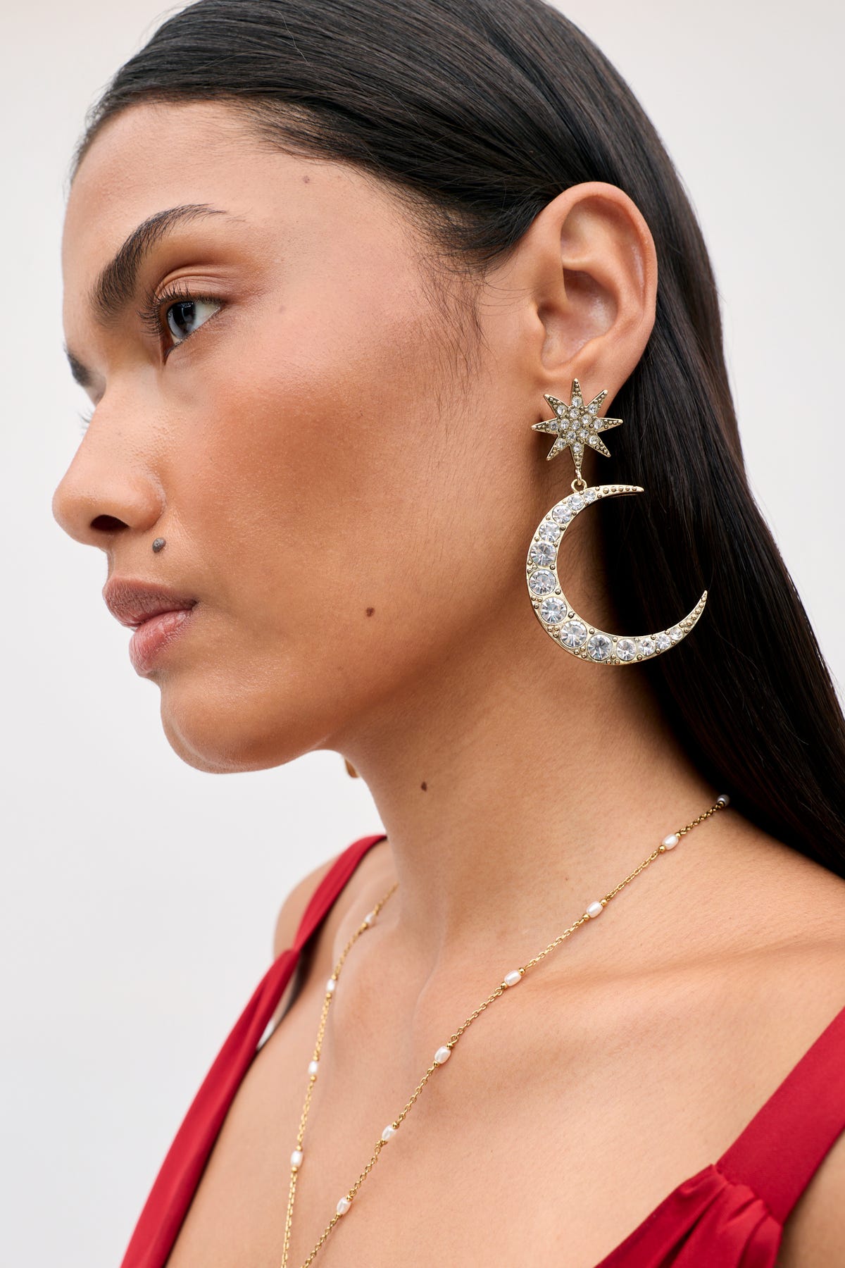 A person wearing the Theresa - Gold earring, featuring a crystal-studded star stud attached to a crescent moon pendant.