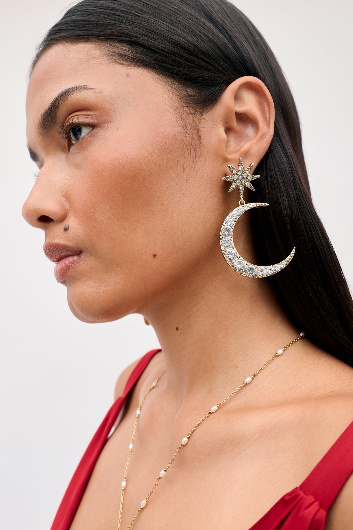 A person wearing the Theresa - Gold earring, featuring a crystal-studded star stud attached to a crescent moon pendant.