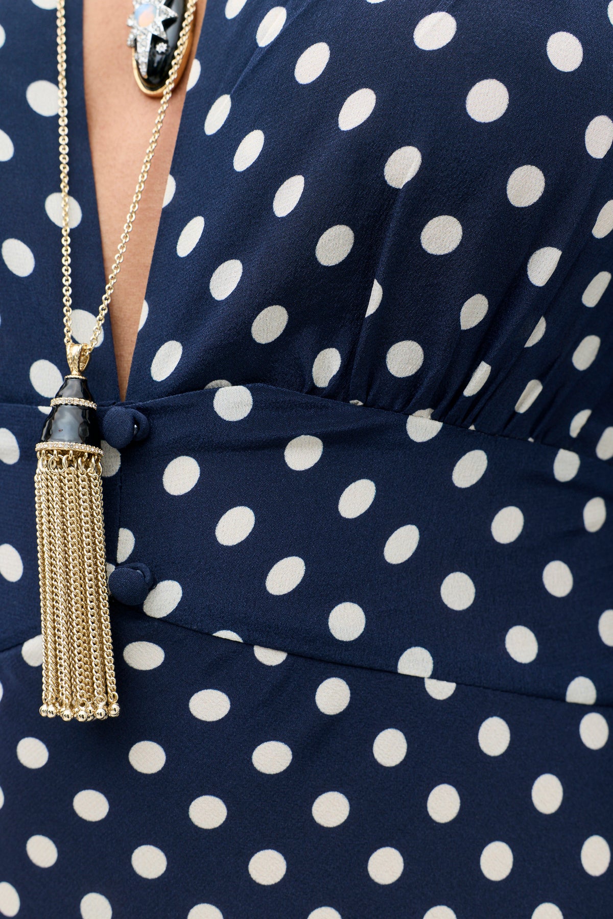 The Lizbeth - Gold chain necklace with a black and gold tassel pendant worn over a navy blue polka dot dress.